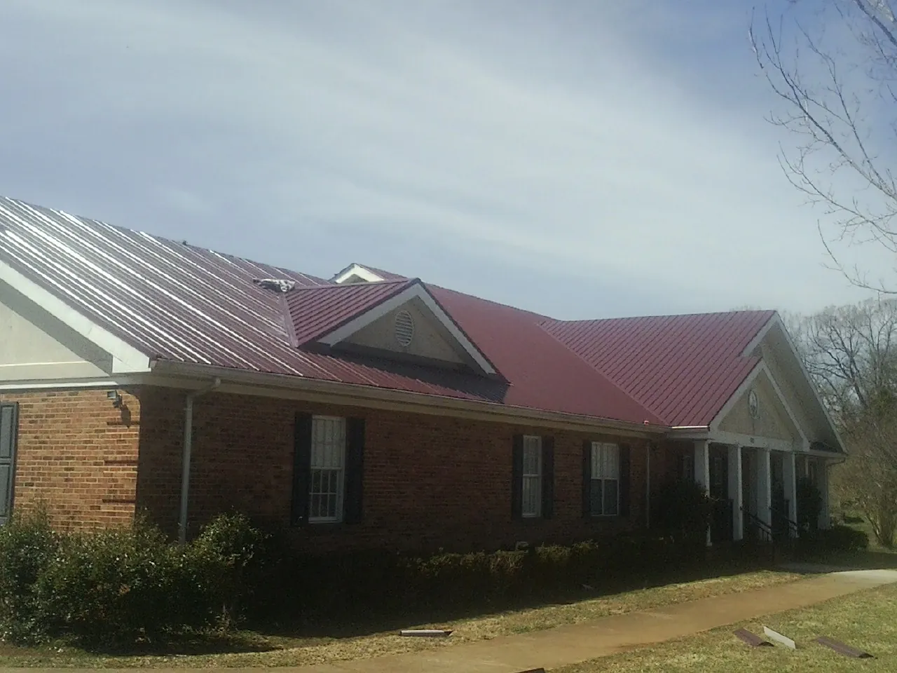 Red metal roof with gabled entries on a long brick building, from a Hail Damage Roof Repair job in Delta